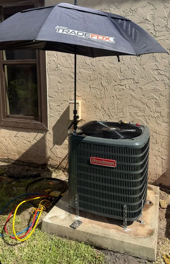 Goodman condenser unit installed outdoors, shaded by a service umbrella during installation