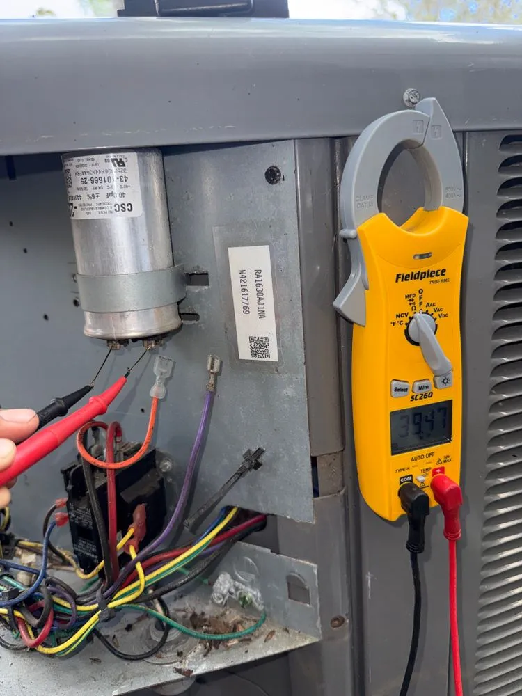 Clamp meter testing a capacitor inside an open condenser electrical panel