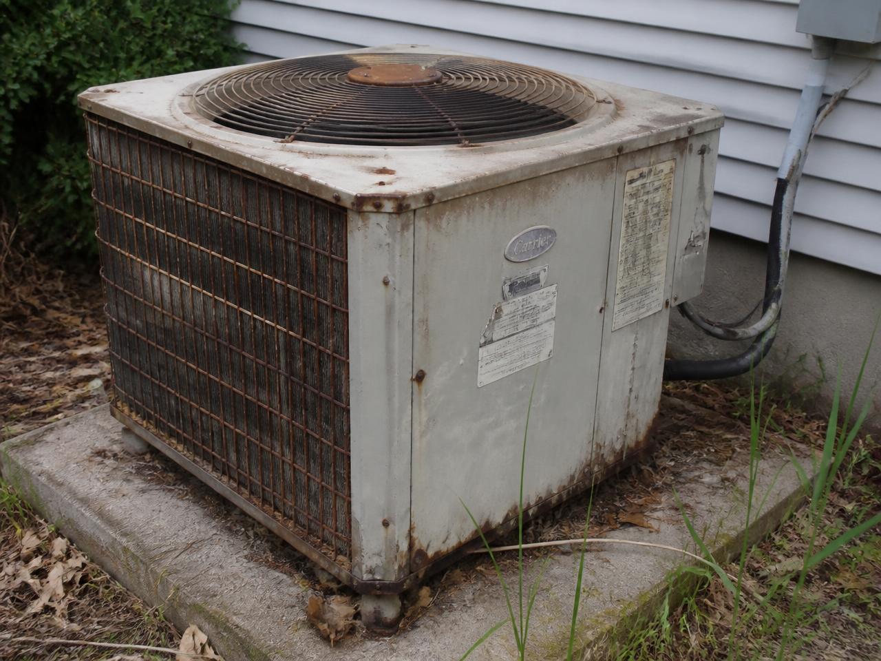 Old rusted outdoor AC condenser unit with bent fins and a dented panel